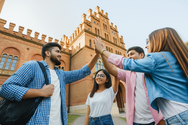 A group of happy Indian college students high-fiving in front of a grand university building, symbolizing unity and achievement, representing the benefits of studying abroad in diverse cultural and academic environments.